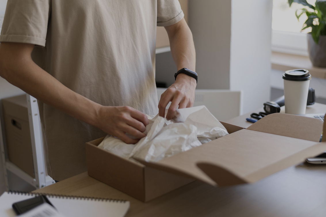 Persoon die een online bestelling inpakt in een kartonnen verzenddoos op een bureau